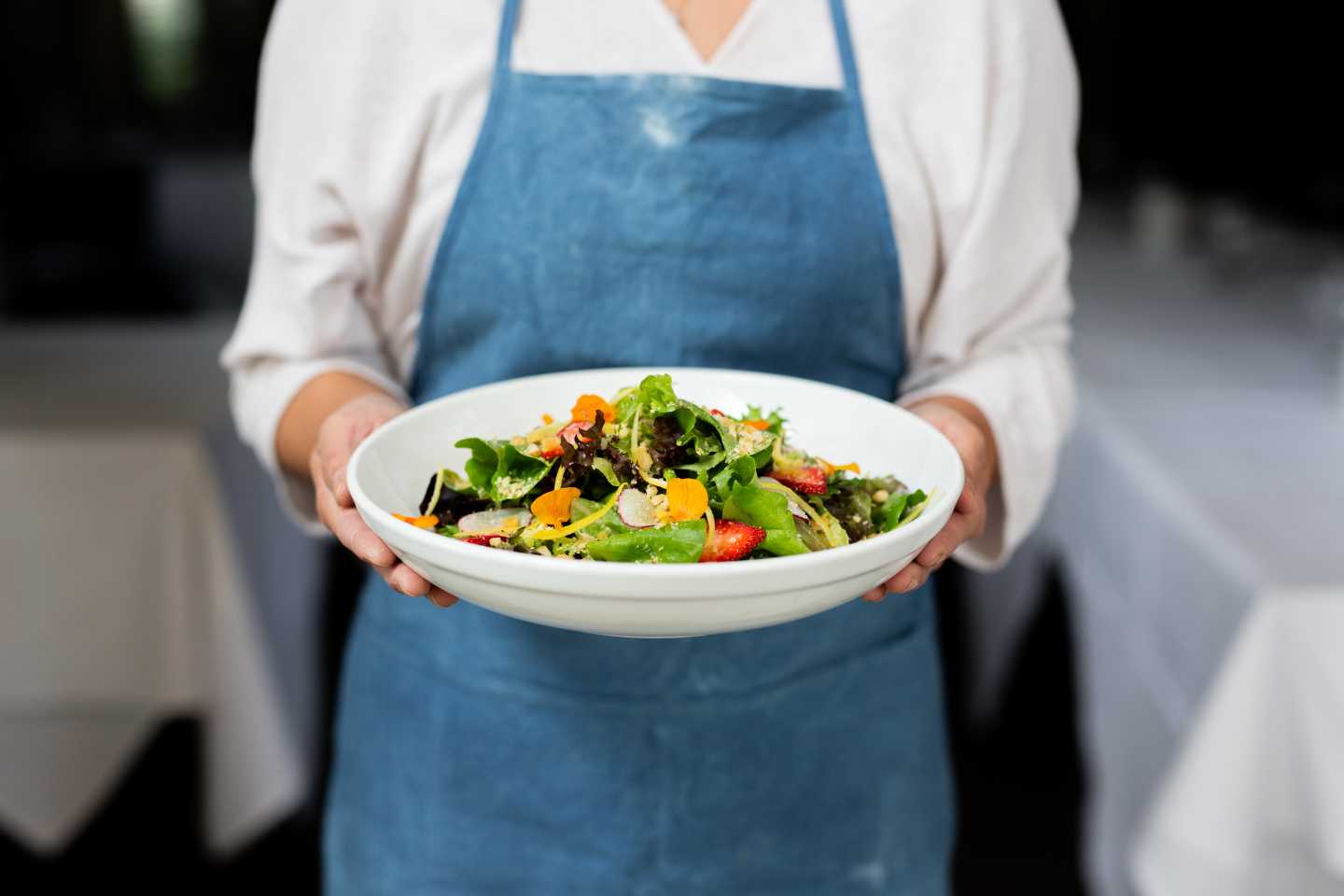 A chef holding a large plate of healthy salad.