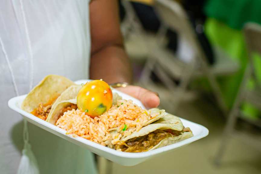 An employee holding a plat containing delicious tacos and rice.
