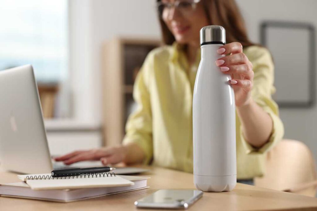 A woman at an office is reaching for a water bottle while working at her computer. Office water service - First Capital Refreshments